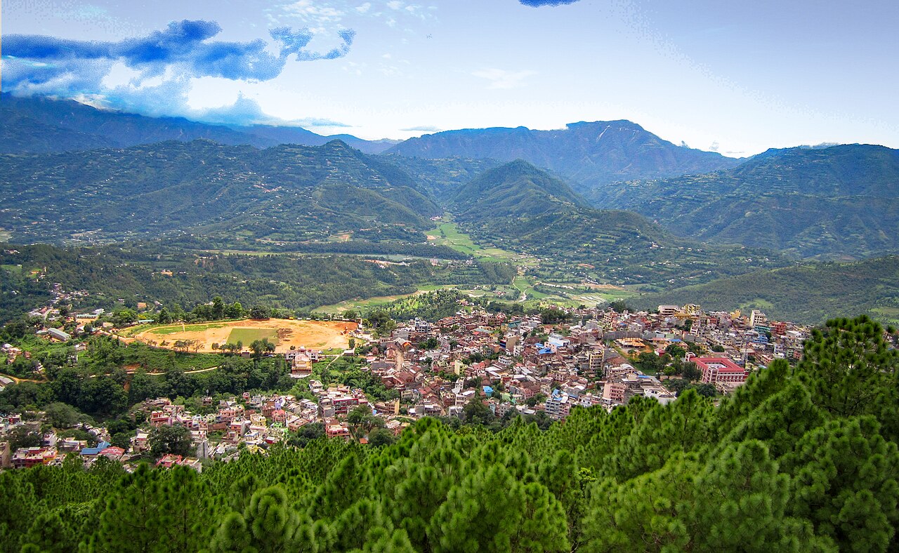 This is a photo of a natural site in Nepal. A small town nestled between a forest and the mountains. 