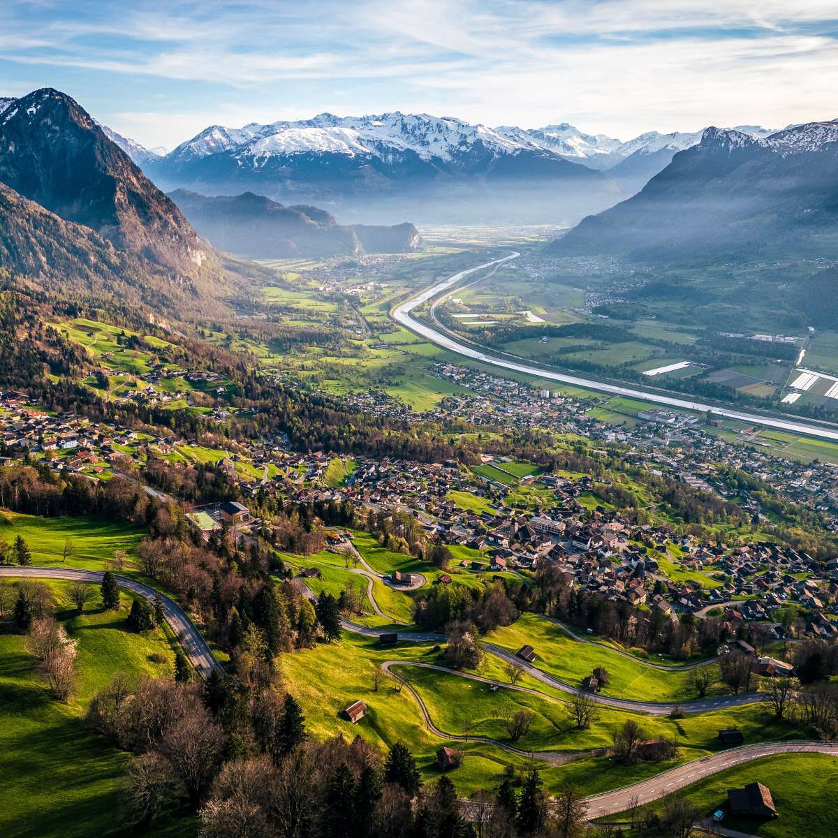 Green hills with winding roads, with mountains in the background