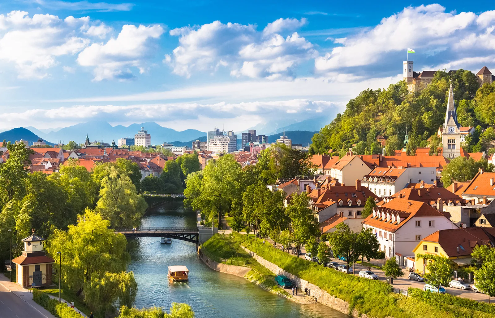 Ljubljana, Slovenia. There is a bridge over Ljubljanica River and old red roofed buildings on either side. 